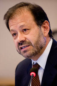 A man in a suit speaks into a microphone in a public forum